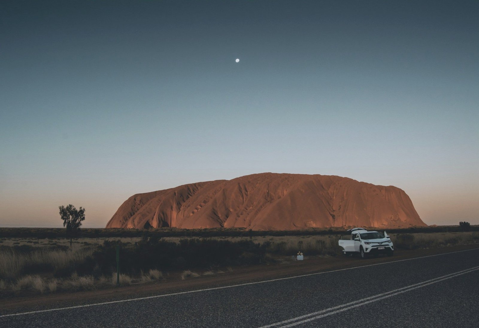 Uluru at dusk with a car on the outback road