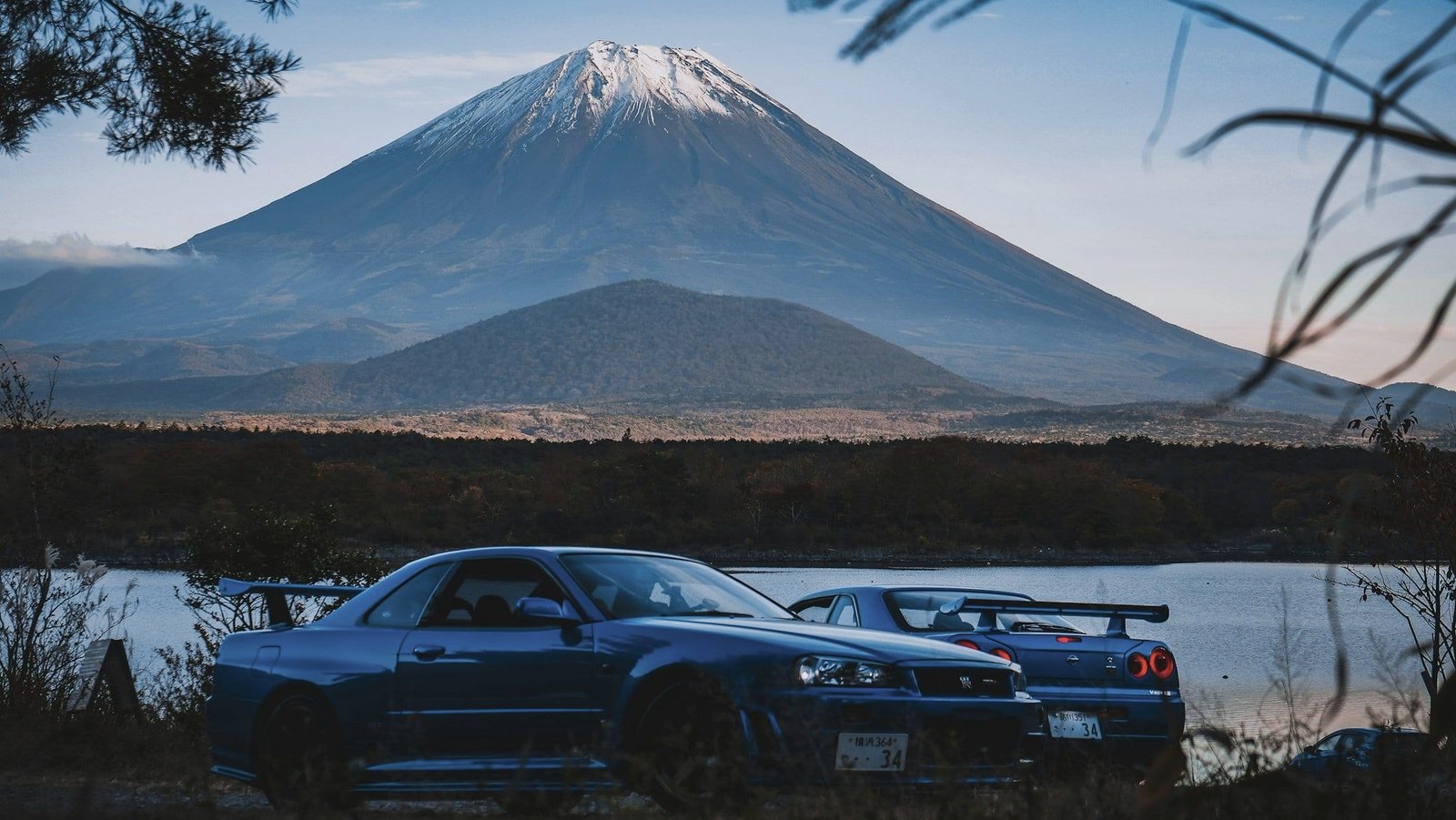 Two Nissan Skyline GT-Rs by a lake with Mount Fuji behind