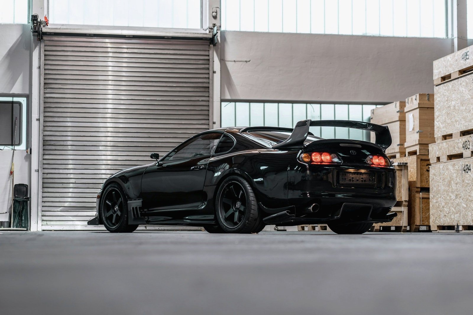 Black Toyota Supra with a rear wing in a warehouse